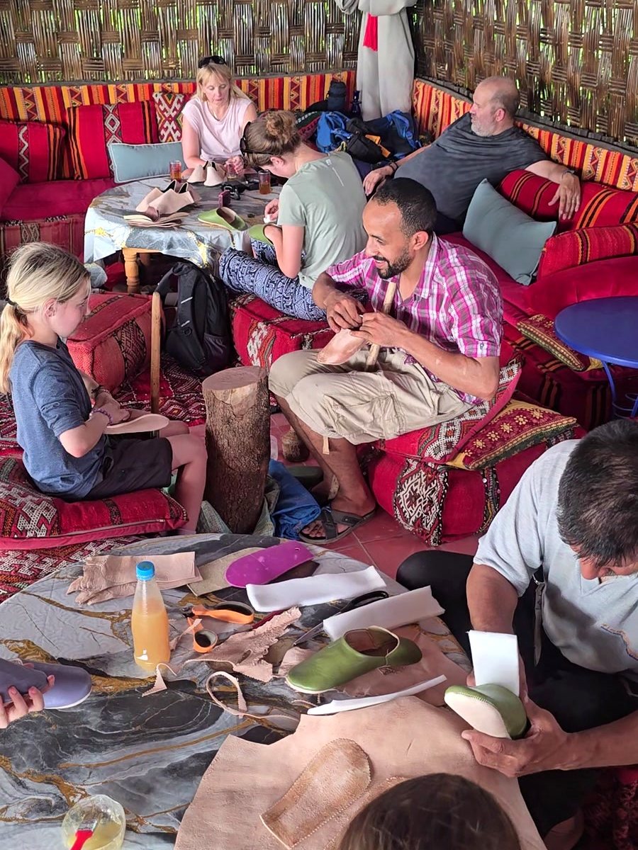 A craftsman guiding a young guest as she shapes her babouche