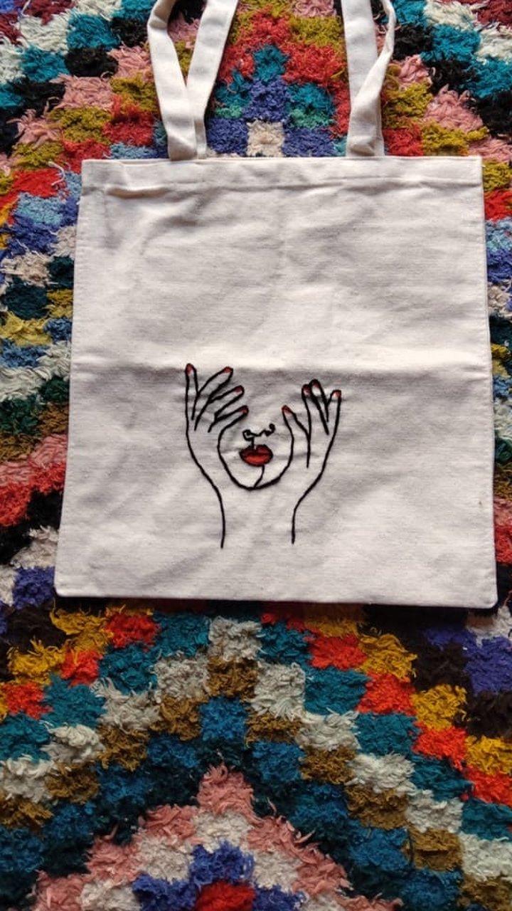 An embroidered tote bag with a line-art face design